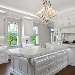 This is an example of an expansive traditional l-shaped kitchen in Sydney with a farmhouse sink, white cabinets, marble benchtops, white splashback, marble splashback, stainless steel appliances, dark hardwood floors, with island, brown floor, white benchtop and shaker cabinets.