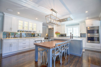Example of a large transitional single-wall medium tone wood floor and brown floor eat-in kitchen design in New York with a farmhouse sink, shaker cabinets, white cabinets, quartz countertops, black backsplash, mirror backsplash, stainless steel appliances, an island and white countertops