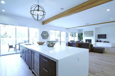 Example of a mid-sized minimalist galley light wood floor and brown floor open concept kitchen design in Los Angeles with flat-panel cabinets, dark wood cabinets, marble countertops, white backsplash, an island, an undermount sink, subway tile backsplash and stainless steel appliances