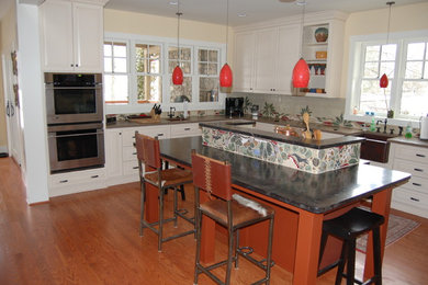 Example of an eclectic kitchen design in Charlotte with a farmhouse sink, raised-panel cabinets, white cabinets, stainless steel appliances and an island