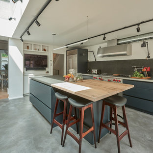 Medium sized industrial l-shaped kitchen in London with flat-panel cabinets, grey cabinets, concrete worktops, black splashback, stainless steel appliances, concrete flooring, an island, grey floors and grey worktops.