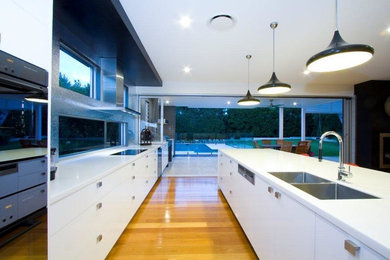 Zweizeilige, Mittelgroße Moderne Wohnküche mit Unterbauwaschbecken, weißen Schränken, Quarzwerkstein-Arbeitsplatte, schwarzen Elektrogeräten, hellem Holzboden, Kücheninsel, flächenbündigen Schrankfronten und Rückwand-Fenster in Brisbane