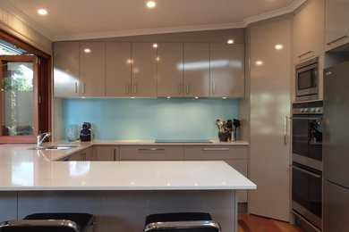 Mittelgroße Moderne Wohnküche in U-Form mit Einbauwaschbecken, Quarzwerkstein-Arbeitsplatte, Küchenrückwand in Blau, Glasrückwand, Küchengeräten aus Edelstahl und braunem Holzboden in Brisbane