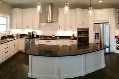 Large trendy l-shaped dark wood floor and brown floor eat-in kitchen photo in Other with an undermount sink, flat-panel cabinets, white cabinets, granite countertops, white backsplash, subway tile backsplash, stainless steel appliances and an island