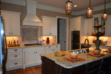 Example of a mid-sized classic u-shaped medium tone wood floor enclosed kitchen design in Nashville with a double-bowl sink, recessed-panel cabinets, white cabinets, granite countertops, white backsplash, stone tile backsplash, stainless steel appliances and an island