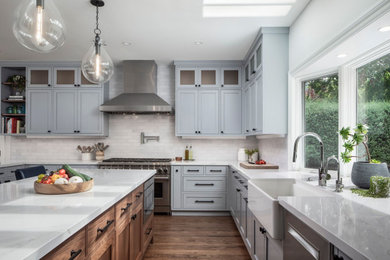 Example of a large transitional u-shaped medium tone wood floor and brown floor open concept kitchen design in San Francisco with a farmhouse sink, shaker cabinets, gray cabinets, quartz countertops, white backsplash, brick backsplash, stainless steel appliances, an island and white countertops