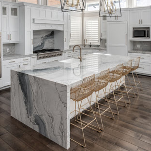 Transitional kitchen pictures - Example of a transitional l-shaped dark wood floor and brown floor kitchen design in Salt Lake City with a farmhouse sink, shaker cabinets, white cabinets, gray backsplash, paneled appliances, an island and gray countertops