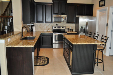 Example of a mid-sized arts and crafts l-shaped ceramic tile and beige floor eat-in kitchen design in Dallas with an undermount sink, recessed-panel cabinets, black cabinets, granite countertops, beige backsplash, stone tile backsplash, stainless steel appliances, an island and beige countertops