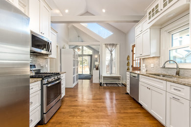 Photo of a large contemporary galley kitchen in Columbus with a submerged sink, shaker cabinets, white cabinets, granite worktops, glass tiled splashback, stainless steel appliances, light hardwood flooring and brown floors.