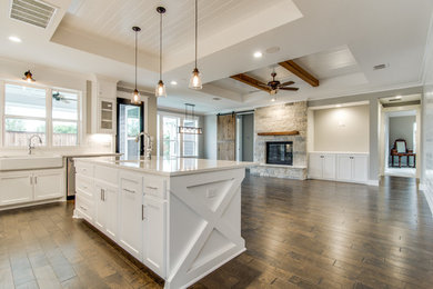 Inspiration for a mid-sized cottage l-shaped dark wood floor and brown floor open concept kitchen remodel in Dallas with a farmhouse sink, shaker cabinets, white cabinets, white backsplash, stainless steel appliances and an island