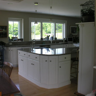 Large traditional l-shaped eat-in kitchen in Portland Maine with an undermount sink, louvered cabinets, white cabinets, granite benchtops, grey splashback, stone slab splashback, white appliances, light hardwood floors and with island.