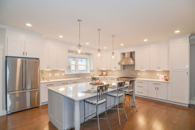 Photo of a large traditional l-shaped kitchen/diner in Boston with a built-in sink, shaker cabinets, white cabinets, engineered stone countertops, grey splashback, ceramic splashback, stainless steel appliances, medium hardwood flooring, an island, brown floors and white worktops.