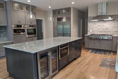 Eat-in kitchen - large contemporary u-shaped light wood floor and brown floor eat-in kitchen idea in Philadelphia with a farmhouse sink, shaker cabinets, gray cabinets, granite countertops, gray backsplash, stone tile backsplash, stainless steel appliances, an island and gray countertops
