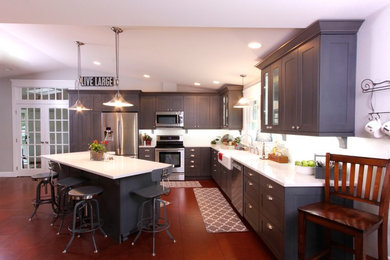 Klassische Wohnküche in L-Form mit Landhausspüle, Schrankfronten im Shaker-Stil, grauen Schränken, Quarzit-Arbeitsplatte, Küchengeräten aus Edelstahl, dunklem Holzboden, Kücheninsel und braunem Boden in Seattle