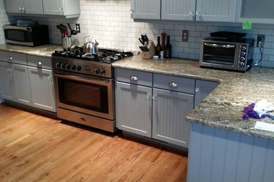 Example of a mid-sized transitional single-wall medium tone wood floor enclosed kitchen design in Charlotte with shaker cabinets, gray cabinets, granite countertops, white backsplash, subway tile backsplash, stainless steel appliances and a peninsula
