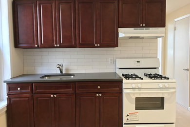 Inspiration for a mid-sized timeless u-shaped porcelain tile and beige floor enclosed kitchen remodel in New York with an undermount sink, raised-panel cabinets, dark wood cabinets, solid surface countertops, white backsplash, subway tile backsplash and stainless steel appliances