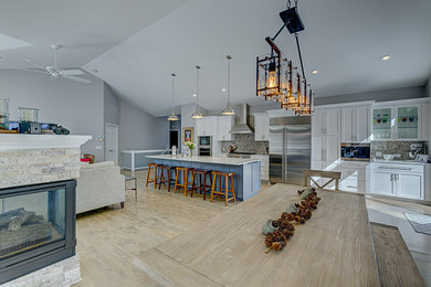 Inspiration for a mid-sized transitional single-wall light wood floor and brown floor eat-in kitchen remodel in Minneapolis with a farmhouse sink, shaker cabinets, white cabinets, quartzite countertops, gray backsplash, stone tile backsplash, stainless steel appliances, an island and white countertops