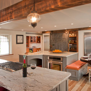 This is an example of a large eclectic u-shaped open plan kitchen in Manchester with a farmhouse sink, flat-panel cabinets, grey cabinets, granite benchtops, stainless steel appliances, light hardwood floors and multiple islands.