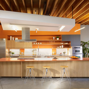 Design ideas for a contemporary galley eat-in kitchen in Los Angeles with a farmhouse sink, flat-panel cabinets, light wood cabinets, orange splashback, window splashback, stainless steel appliances, concrete floors, with island, grey floor and orange benchtop.