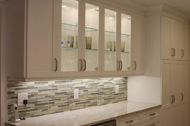 Transitional galley medium tone wood floor enclosed kitchen photo in New York with recessed-panel cabinets, white cabinets, quartz countertops, multicolored backsplash, glass tile backsplash, stainless steel appliances and an island