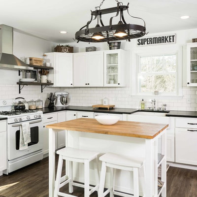 Inspiration for a mid-sized farmhouse l-shaped vinyl floor and brown floor kitchen remodel in Portland Maine with a farmhouse sink, shaker cabinets, white cabinets, granite countertops, white backsplash, subway tile backsplash, white appliances and an island