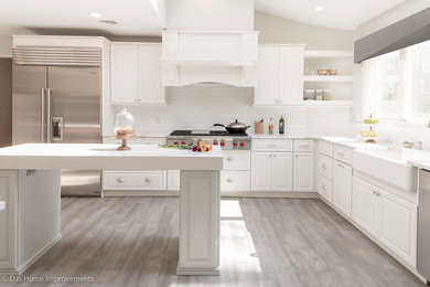 Inspiration for a large transitional l-shaped ceramic tile and gray floor eat-in kitchen remodel in New York with a farmhouse sink, raised-panel cabinets, white cabinets, quartz countertops, white backsplash, porcelain backsplash, stainless steel appliances and an island