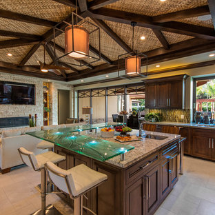 Tropical open concept kitchen appliance - Open concept kitchen - tropical u-shaped travertine floor open concept kitchen idea in San Diego with recessed-panel cabinets, dark wood cabinets, granite countertops, green backsplash, glass tile backsplash and an island