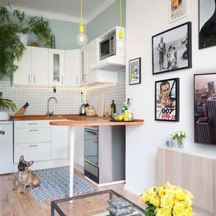 Design ideas for a small scandi l-shaped open plan kitchen in London with a submerged sink, shaker cabinets, white cabinets, wood worktops, white splashback, ceramic splashback, stainless steel appliances, laminate floors and a breakfast bar.