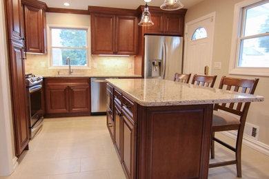Small transitional l-shaped beige floor enclosed kitchen photo in New York with an undermount sink, raised-panel cabinets, brown cabinets, quartzite countertops, stainless steel appliances, an island, beige countertops and gray backsplash