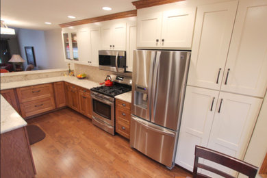 Example of a mid-sized trendy l-shaped medium tone wood floor and brown floor open concept kitchen design in Cleveland with an undermount sink, shaker cabinets, white cabinets, marble countertops, beige backsplash, glass tile backsplash and stainless steel appliances