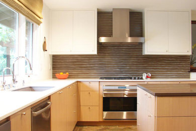 Inredning av ett stort l-kök, med en undermonterad diskho, släta luckor, skåp i ljust trä, brunt stänkskydd, rostfria vitvaror, klinkergolv i terrakotta och en köksö