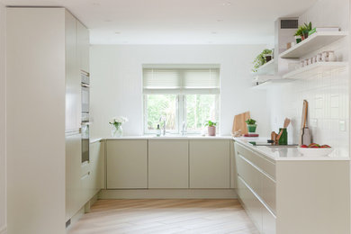 Photo of a scandi u-shaped enclosed kitchen in Cambridgeshire with flat-panel cabinets, beige cabinets, ceramic splashback, integrated appliances, light hardwood flooring, no island, beige floors and white worktops.