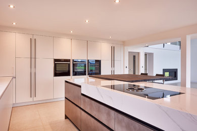 This is an example of an expansive contemporary l-shaped open plan kitchen in West Midlands with flat-panel cabinets, white cabinets, composite countertops, porcelain flooring, an island and beige floors.