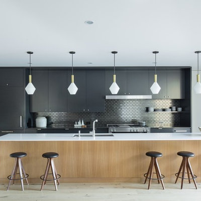 Open concept kitchen - mid-century modern galley light wood floor and beige floor open concept kitchen idea in Portland with an undermount sink, flat-panel cabinets, black cabinets, metallic backsplash, mosaic tile backsplash, paneled appliances, an island and white countertops