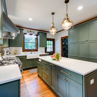 Mid-sized arts and crafts l-shaped kitchen in Oklahoma City with a farmhouse sink, shaker cabinets, green cabinets, quartz benchtops, yellow splashback, ceramic splashback, stainless steel appliances, medium hardwood floors, with island, brown floor and white benchtop.