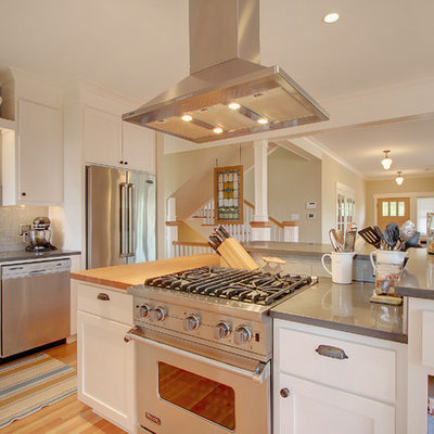 Example of a mid-sized arts and crafts l-shaped light wood floor eat-in kitchen design in Seattle with stainless steel appliances, a farmhouse sink, recessed-panel cabinets, white cabinets, gray backsplash, subway tile backsplash and an island