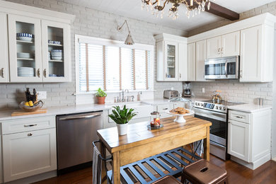 Large mountain style l-shaped dark wood floor and brown floor enclosed kitchen photo in Other with a farmhouse sink, recessed-panel cabinets, white cabinets, quartzite countertops, gray backsplash, stainless steel appliances, an island and subway tile backsplash