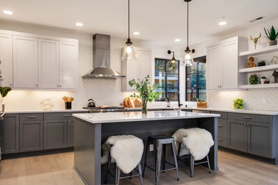 Large transitional l-shaped light wood floor and brown floor eat-in kitchen photo in Seattle with an undermount sink, shaker cabinets, gray cabinets, white backsplash, porcelain backsplash, stainless steel appliances, an island, white countertops and granite countertops