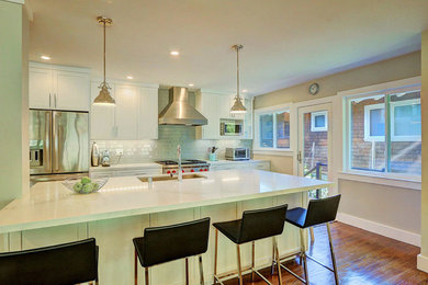 Bild på ett stort funkis linjärt kök och matrum, med en nedsänkt diskho, skåp i shakerstil, vita skåp, laminatbänkskiva, vitt stänkskydd, stänkskydd i tunnelbanekakel, rostfria vitvaror, mellanmörkt trägolv och en köksö