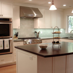 This is an example of a mid-sized traditional l-shaped open plan kitchen in San Francisco with a drop-in sink, shaker cabinets, white cabinets, green splashback, light hardwood floors, with island, granite benchtops, glass tile splashback, stainless steel appliances, brown floor and green benchtop.