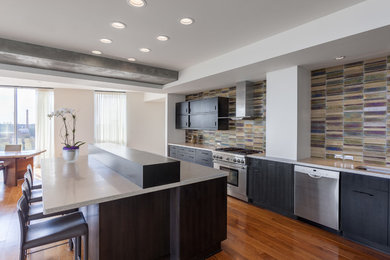 Example of a trendy galley medium tone wood floor kitchen design in Raleigh with black cabinets, multicolored backsplash, glass tile backsplash, stainless steel appliances and an island