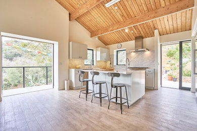 Eat-in kitchen - mid-sized transitional u-shaped porcelain tile and beige floor eat-in kitchen idea in Los Angeles with a farmhouse sink, flat-panel cabinets, white cabinets, quartz countertops, white backsplash, stone slab backsplash, stainless steel appliances and an island