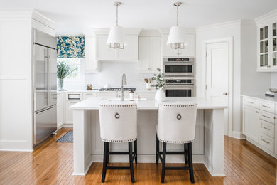 Kitchen - mid-sized traditional u-shaped medium tone wood floor and brown floor kitchen idea in Charlotte with a farmhouse sink, shaker cabinets, white cabinets, quartz countertops, gray backsplash, porcelain backsplash, stainless steel appliances, an island and white countertops