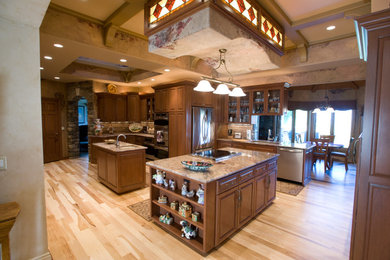 Example of a classic u-shaped eat-in kitchen design in Omaha with an undermount sink, raised-panel cabinets, medium tone wood cabinets, granite countertops, brown backsplash, stone tile backsplash and stainless steel appliances