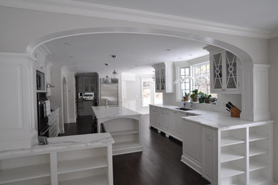 Bild på ett stort vintage kök, med en undermonterad diskho, luckor med glaspanel, vita skåp, marmorbänkskiva, vitt stänkskydd, stänkskydd i tunnelbanekakel, rostfria vitvaror, mörkt trägolv, en köksö och brunt golv