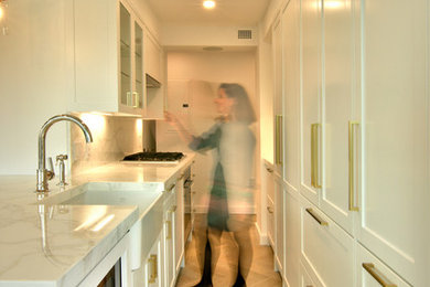 ニューヨークにある高級な小さなトランジショナルスタイルのおしゃれなキッチン (アンダーカウンターシンク、シェーカースタイル扉のキャビネット、白いキャビネット、大理石カウンター、白いキッチンパネル、石スラブのキッチンパネル、パネルと同色の調理設備、淡色無垢フローリング、ベージュの床、白いキッチンカウンター) の写真