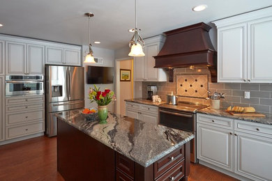 Klassisk inredning av ett mellanstort kök, med en undermonterad diskho, luckor med upphöjd panel, vita skåp, granitbänkskiva, grått stänkskydd, stänkskydd i cementkakel, rostfria vitvaror, mellanmörkt trägolv och flera köksöar
