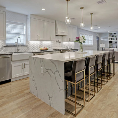 Example of a mid-sized transitional galley light wood floor and yellow floor eat-in kitchen design in Houston with a farmhouse sink, recessed-panel cabinets, white cabinets, quartz countertops, white backsplash, ceramic backsplash, stainless steel appliances, an island and white countertops