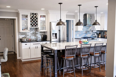 Large trendy u-shaped light wood floor and brown floor eat-in kitchen photo in Columbus with a single-bowl sink, shaker cabinets, white cabinets, granite countertops, gray backsplash, glass tile backsplash, stainless steel appliances and an island