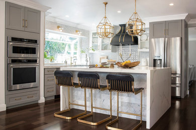 Transitional l-shaped dark wood floor and brown floor kitchen photo in Orange County with a farmhouse sink, shaker cabinets, gray cabinets, gray backsplash, stainless steel appliances and an island